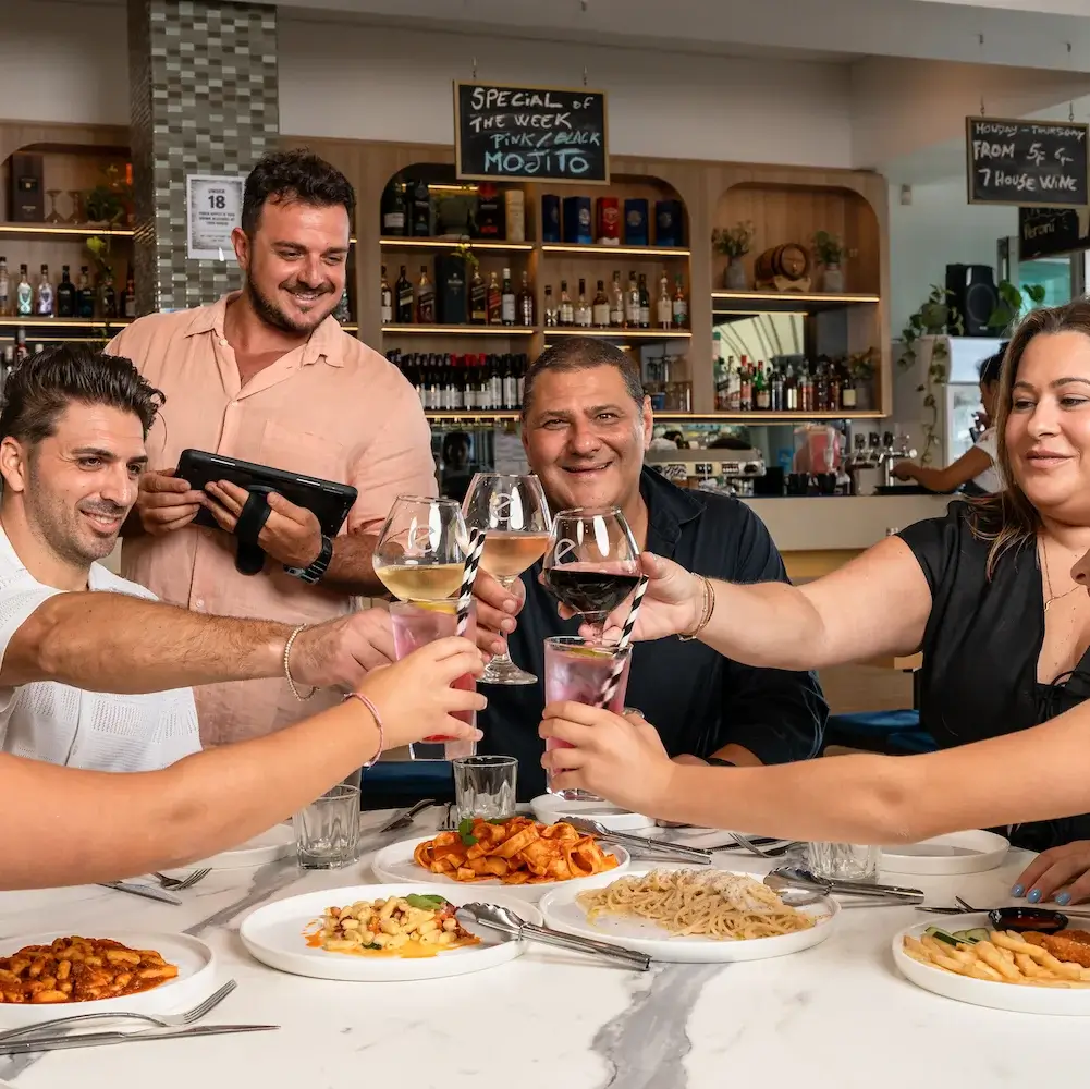 Friends toasting with drinks over Italian pasta dishes at Enzo’s Cucina restaurant.