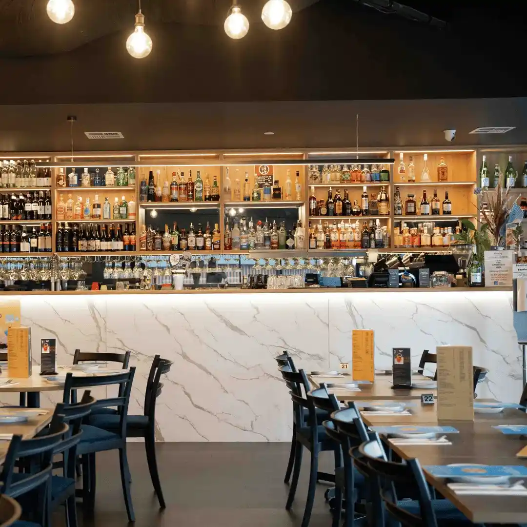 Interior view of Enzos Cucina restaurant bar area featuring backlit liquor shelves, marble counter and dining tables