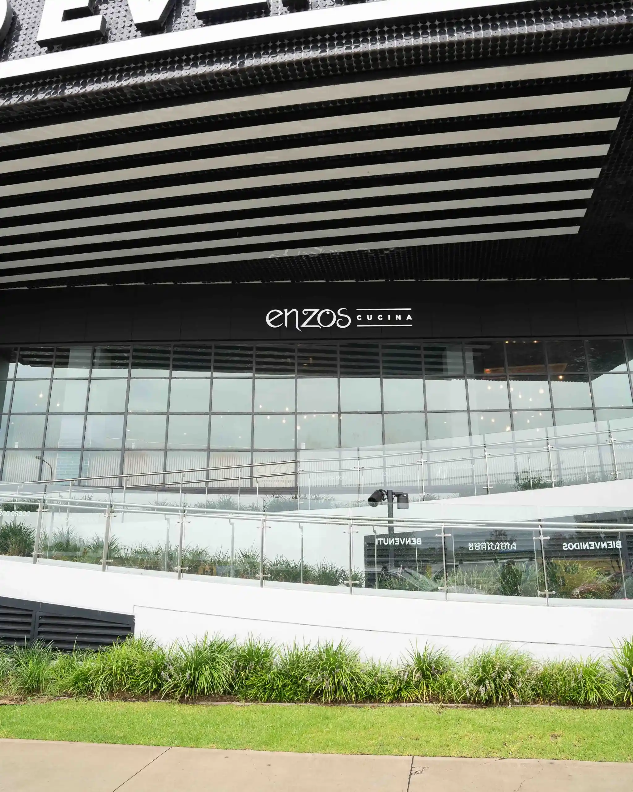 Wide exterior view of Enzos Cucina restaurant with large glass windows and outdoor landscaping
