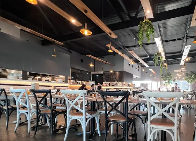 Interior view of Enzos Cucina restaurant featuring rustic wooden tables, cross back chairs and warm hanging lights